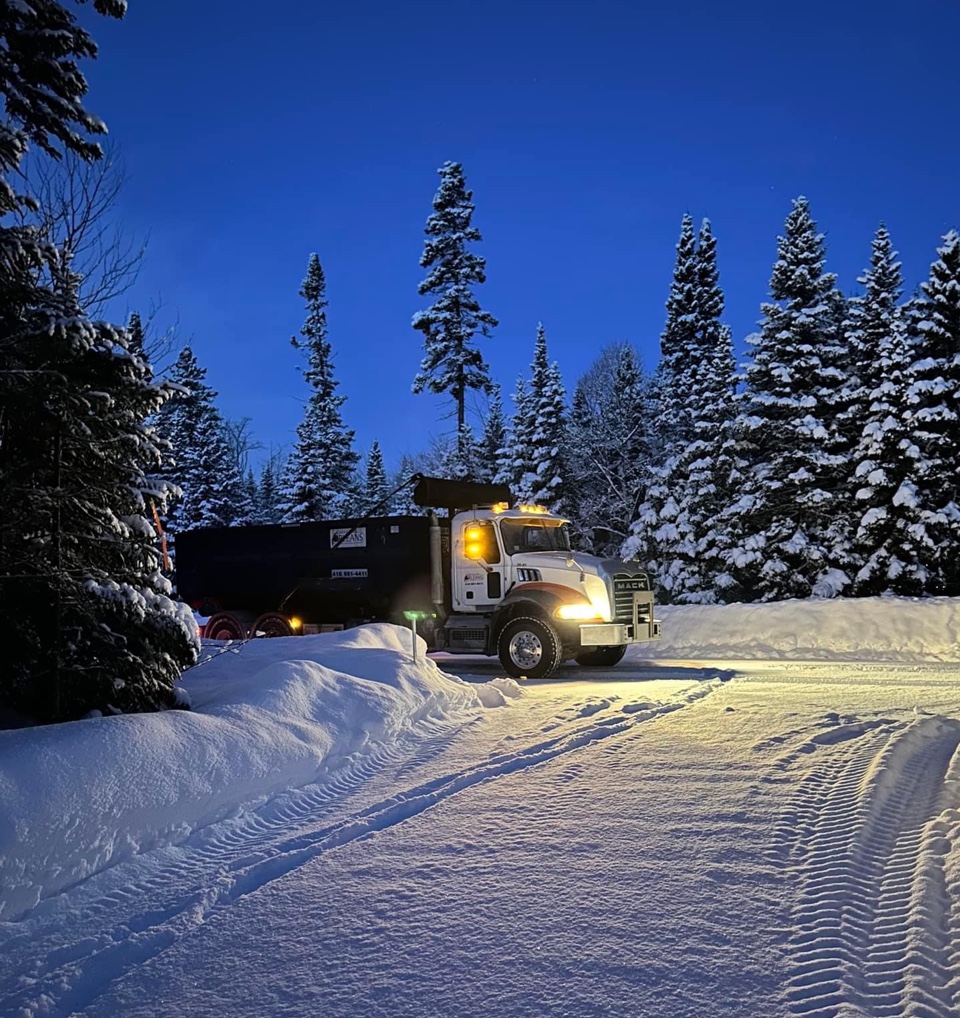 Camion de livraison de conteneur circulant sur un chemin déneigé en hiver, accès dégagé permettant le transport et la collecte malgré la neige.